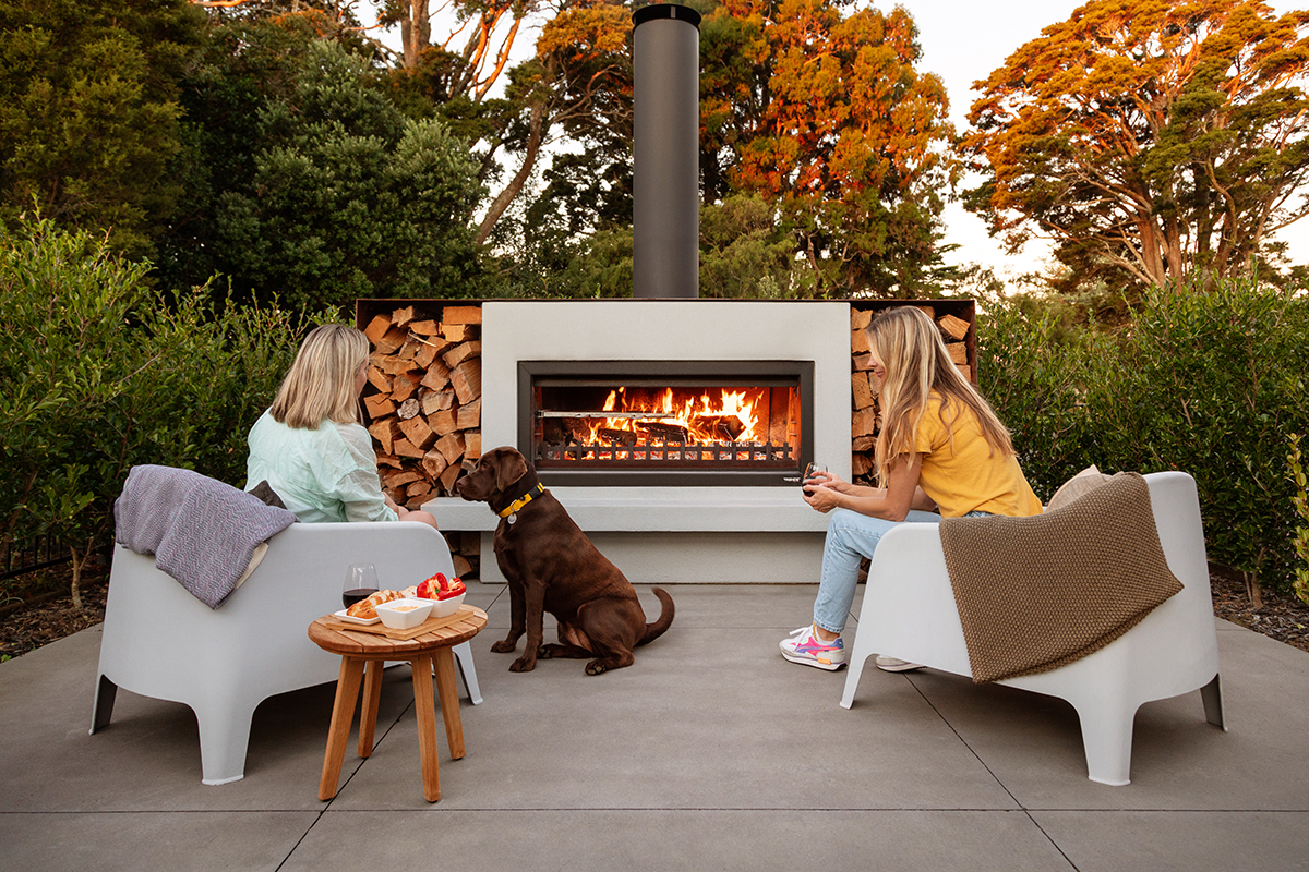 friends sitting in front of an outdoor fireplace in their backyard and a dog, with sunsetting